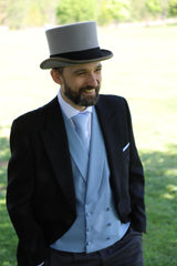 Model wearing ACS Rental black morning suit with sky blue waistcoat, tie and pocket square, with a grey top hat, looking left, smiling with hands in pockets