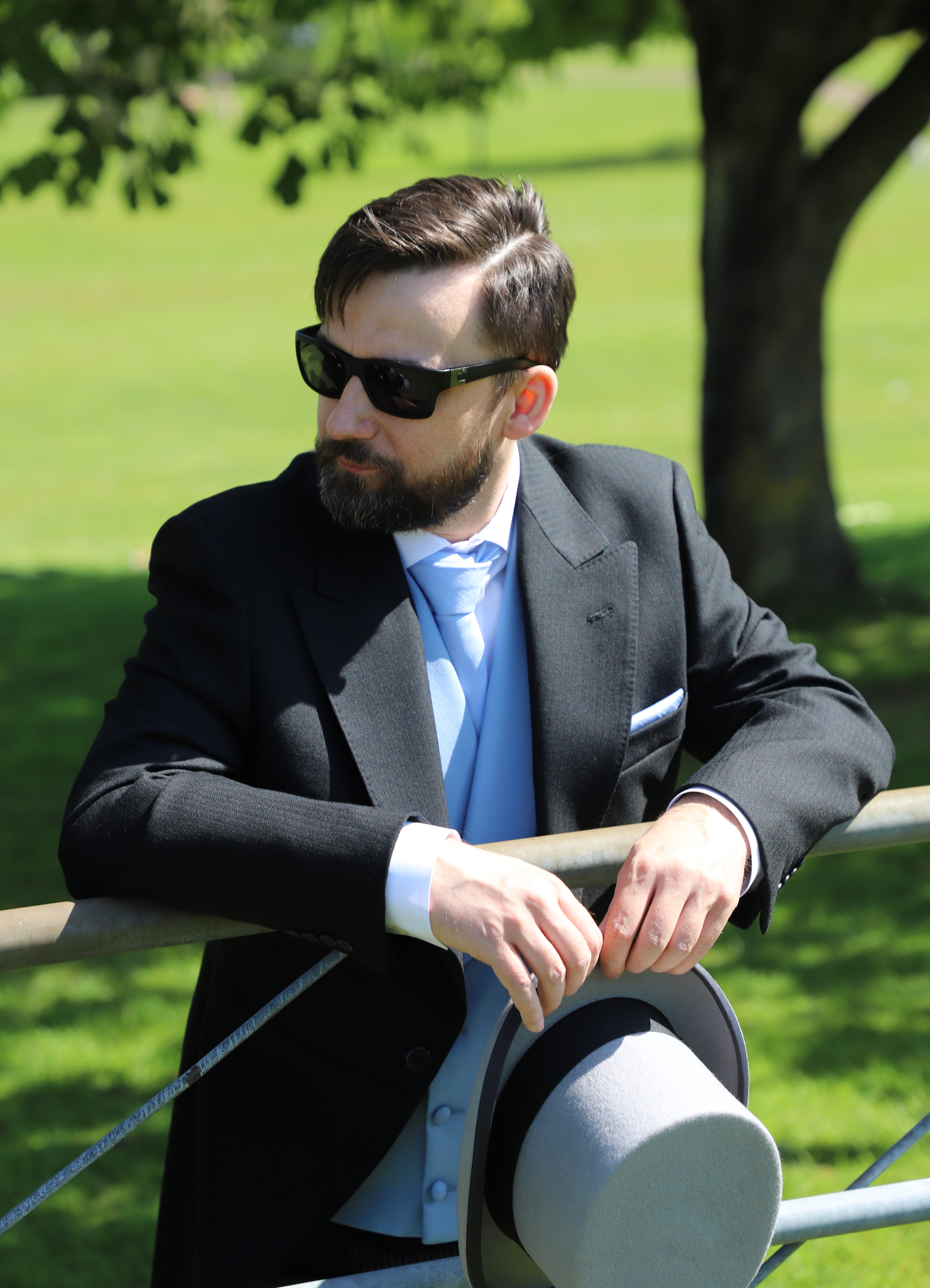 ACS Rental black morning suit with sky blue waistcoat and matching tie and pocket square. Model looks left and holds a grey top hat