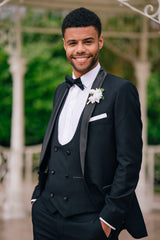 Groom smiling in black slim fit tuxedo, and bow tie outdoors.