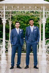 Two groomsmen in Italian blue slim fit suits standing together under a gazebo
