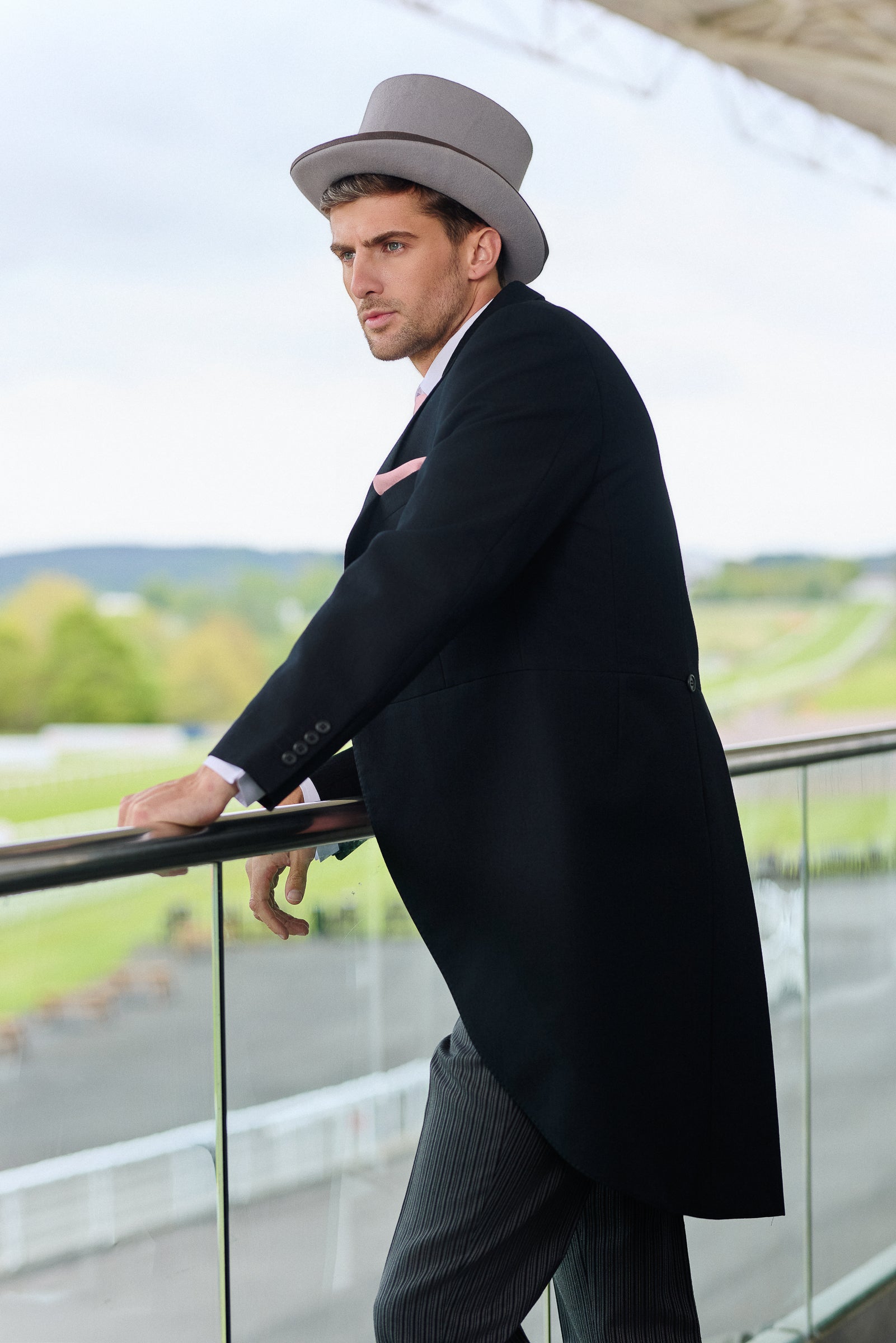 Man in a black tailcoat and grey hat standing on a balcony at Royal Ascot