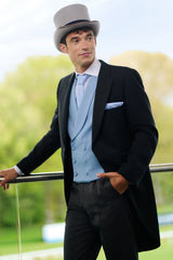 Man in Royal Ascot attire with a top hat standing against a balcony.