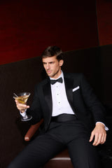Man in a tuxedo holding a cocktail in a dimly lit room