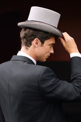 Man adjusting a gray top hat against a dark background