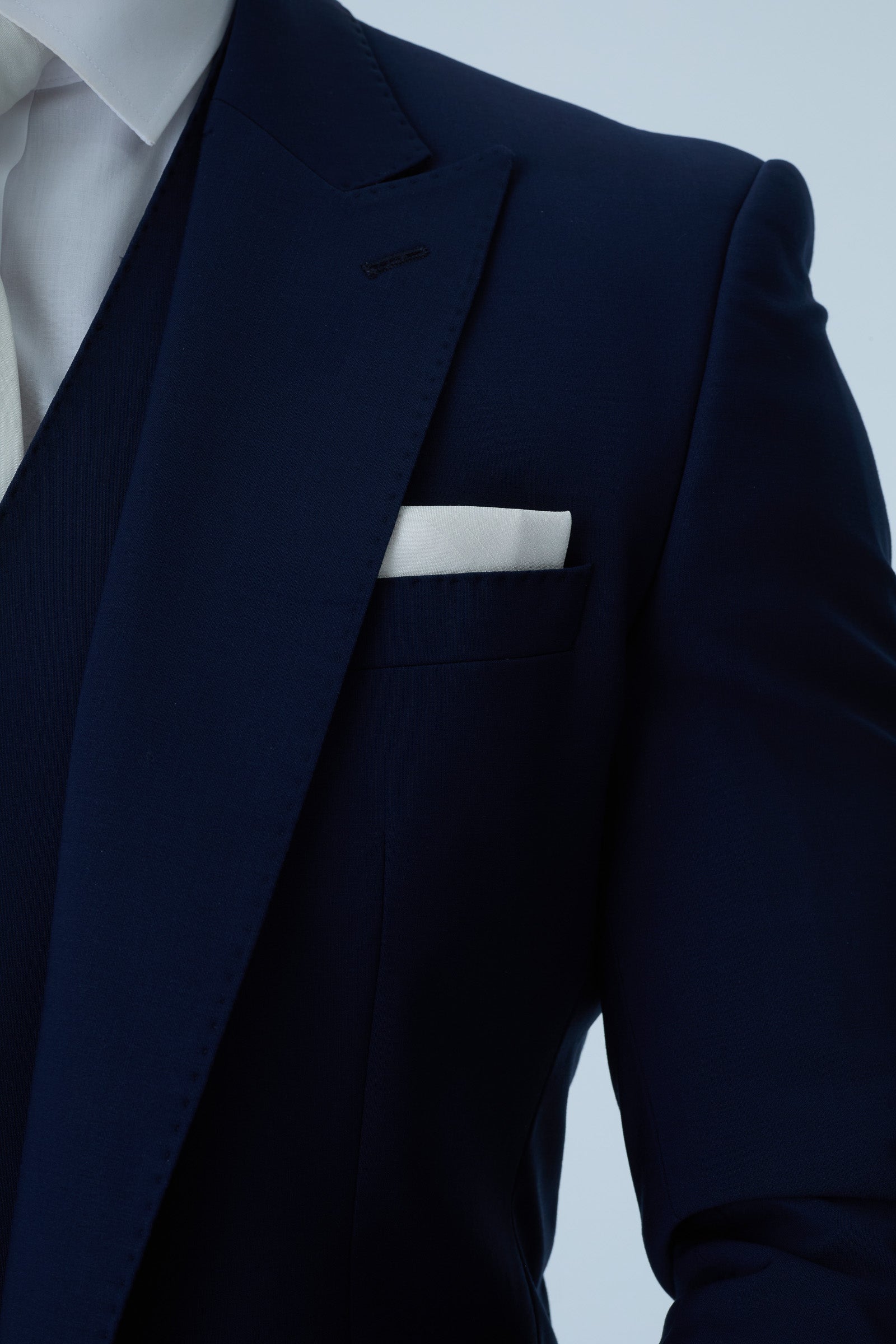 Navy blue suit jacket with a white pocket square on a light gray background