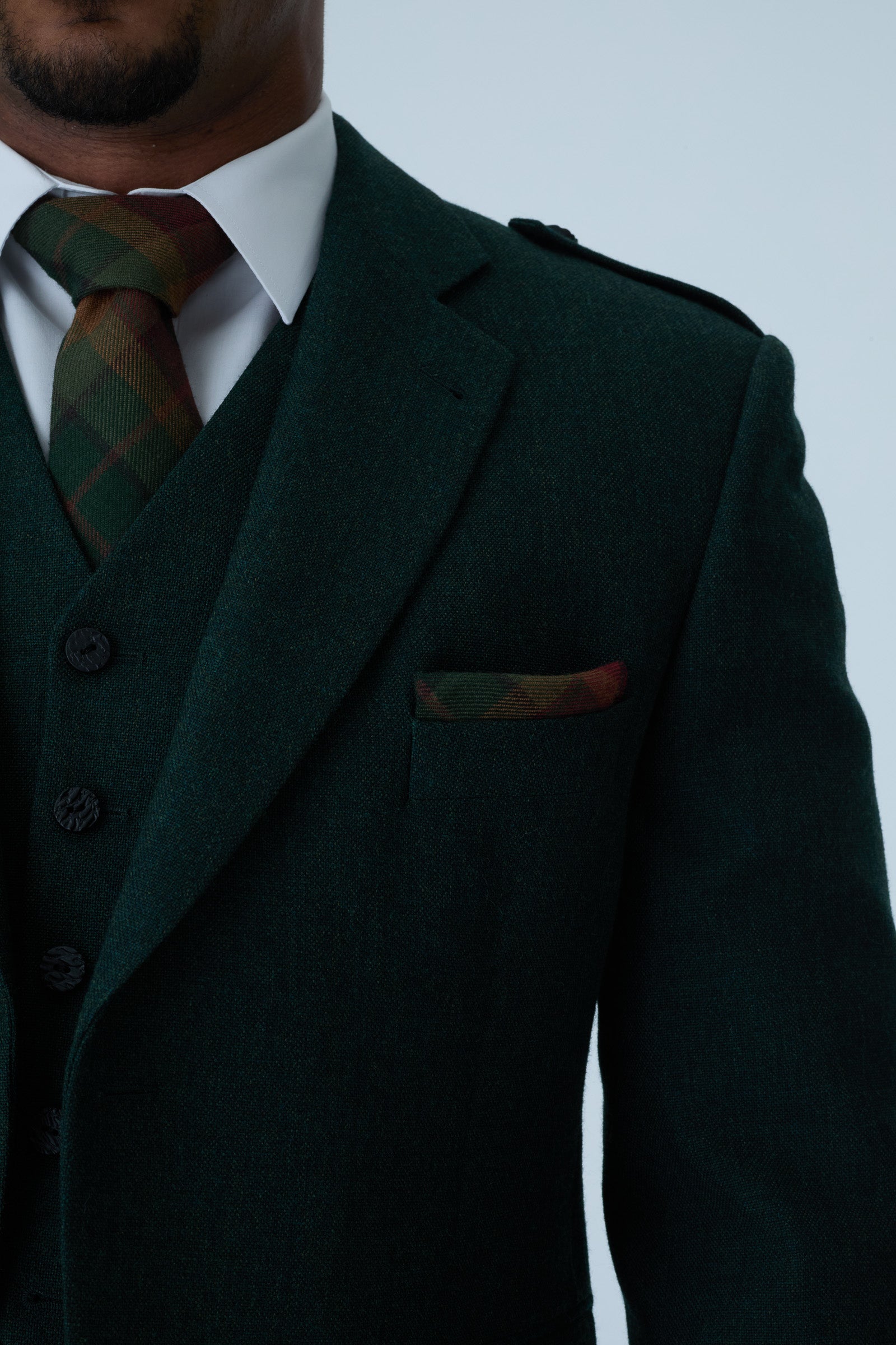 Dark green tweed jacket with tartan tie on a plain background