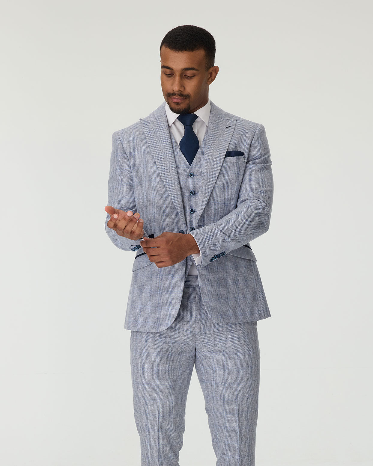 Man wearing a sky blue checkered suit with a white shirt and navy tie on a plain background